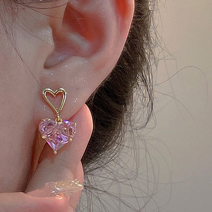 Ein Paar elegante Herzenohrringe mit rosa Kristall und ggoldenen Herzen getragen